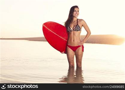 Beautiful surfer girl in the beach with her surfboard at sunset