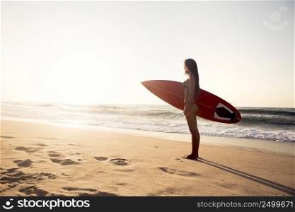 Beautiful surfer girl in the beach with her surfboard at sunset. Surfer Girl