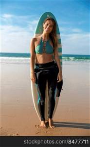 Beautiful surfer girl on the beach with her surfboard and smiling