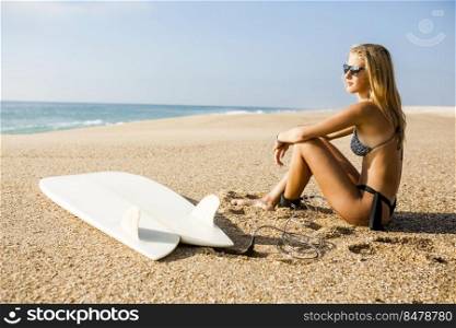 Beautiful surfer girl sitting on the beach and checking the waves