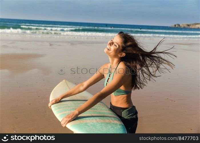 Beautiful surfer girl walking over the beach with her surfboard and smiling