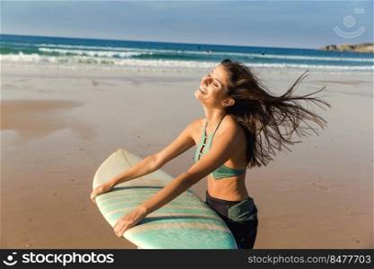 Beautiful surfer girl walking over the beach with her surfboard and smiling