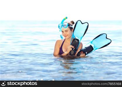 Beautiful tanned girl with mask and snorkel holding flippers chest-deep in water