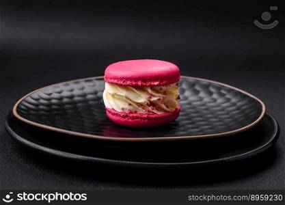 Beautiful tasty macaron with filling and fruit flavor on a black plate on a dark concrete background