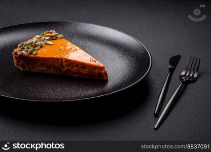 Beautiful tasty pumpkin pie with slices on a black ceramic plate on a dark concrete background