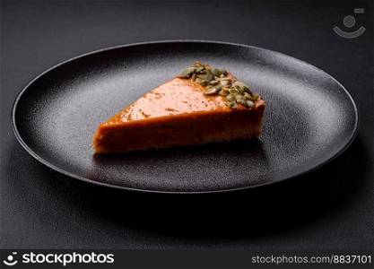 Beautiful tasty pumpkin pie with slices on a black ceramic plate on a dark concrete background
