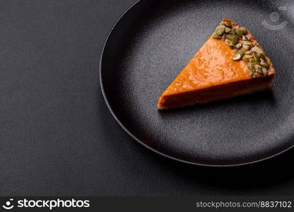 Beautiful tasty pumpkin pie with slices on a black ceramic plate on a dark concrete background