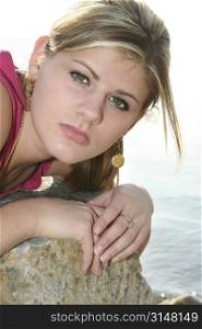 Beautiful teen girl outside by the lake laying on a rock.
