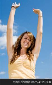 Beautiful teen girl raising her arms in happiness against a vivid blue sky.