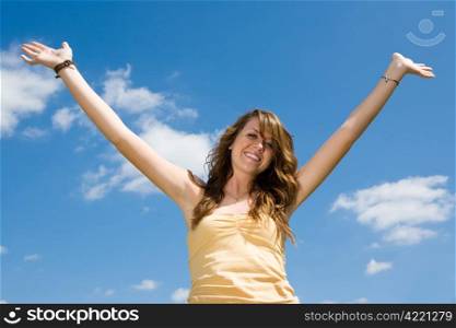 Beautiful teen girl raising her hands in joy and praise against a blue sky.