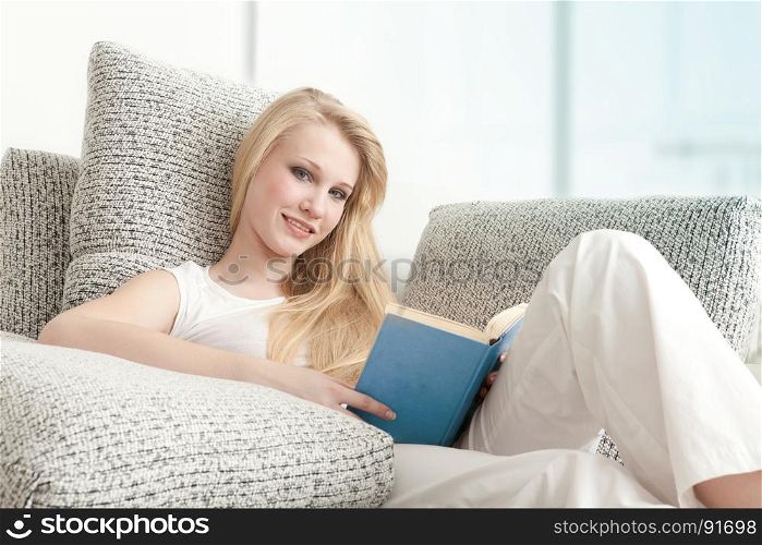 Beautiful Teen Student Reading the Book, Drinking Coffee, Lying on the Sofa in Living Room
