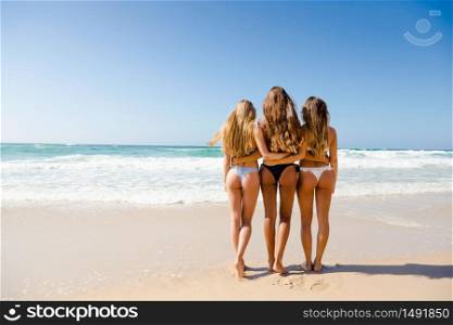 Beautiful teenage friends on the beach embraced together and looking to the sea