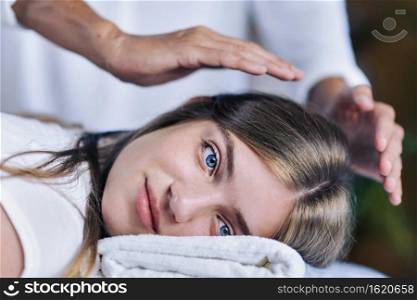 Beautiful teenage girl at Reiki spiritual healing session. Reiki therapist holding hands over patient head and transfer energy. Peaceful teenage girl smiling and lying with her eyes open.