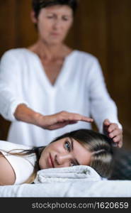 Beautiful teenage girl at Reiki spiritual healing session. Reiki therapist holding hands over patient head and transfer energy. Peaceful teenage girl smiling and lying with her eyes open.