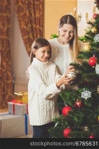 Beautiful teenage girl helping mother decorating Christmas tree