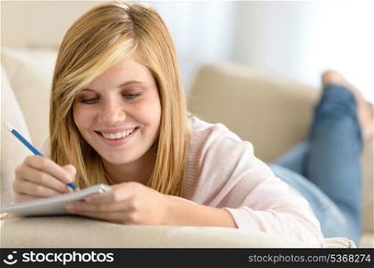 Beautiful teenage girl lying on sofa writing notes in diary