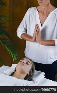 Beautiful teenage girl lying with her eyes closed and having Reiki healing treatment. Reiki Practitioner standing and praying above patient’s body. 