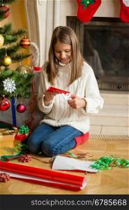 Beautiful teenage girl making paper snowflakes at living room at decorated Christmas tree
