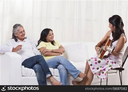 Beautiful teenage girl playing guitar for her mother and grandmother
