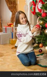 Beautiful teenage girl posing at Christmas tree with red bauble