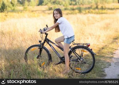 Beautiful teenage girl posing on bicycle in field at hot sunny day