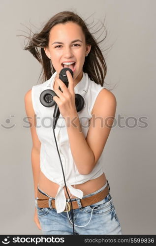 Beautiful teenage girl singing with microphone blowing hair on gray background