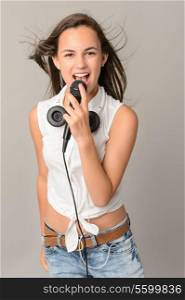 Beautiful teenage girl singing with microphone blowing hair on gray background