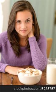 Beautiful teenage girl sitting behind table with cereal breakfast