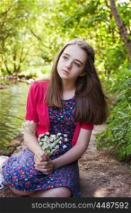 Beautiful teenage girl sitting beside a river holding a bunch of flowers
