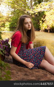 Beautiful teenage girl sitting beside a river lookingg into the distance