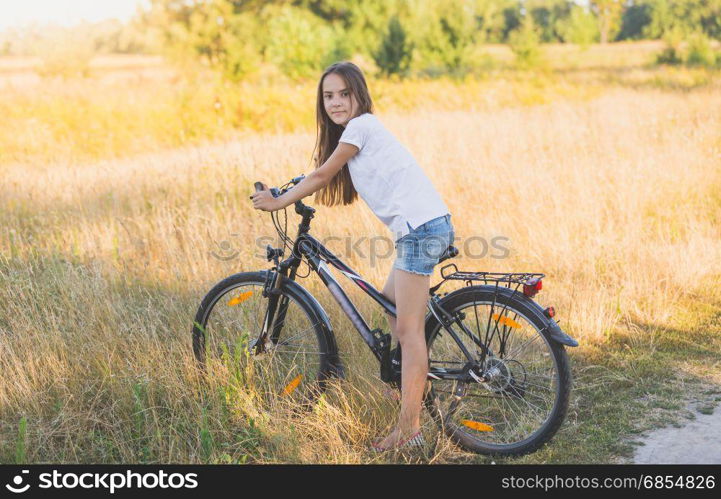 Beautiful teenage girl sitting on bicycle at meadow