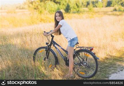 Beautiful teenage girl sitting on bicycle at meadow