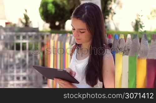 Beautiful teenage girl student using tablet pc in front of the school showing it at camera.