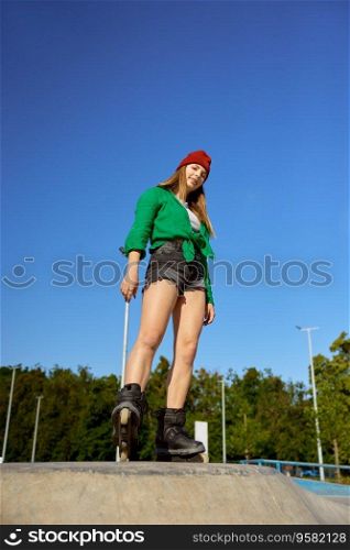 Beautiful teenager girl on roller skates posing for camera over blue sky. Healthy lifestyle and sports activity. Beautiful teenager girl on roller skates posing for camera over blue sky