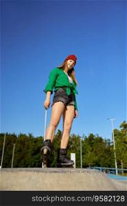 Beautiful teenager girl on roller skates posing for camera over blue sky. Healthy lifestyle and sports activity. Beautiful teenager girl on roller skates posing for camera over blue sky