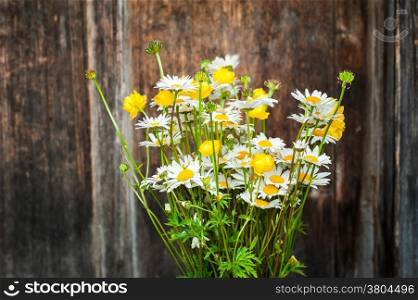 Beautiful tender bouquet of summer meadow flowers with wild chamomiles on wooden background. Floral composition in rural vintage style