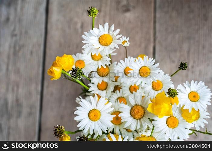Beautiful tender bouquet of summer meadow flowers with wild chamomiles on wooden background. Floral composition in rural vintage style