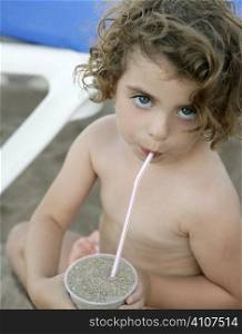 Beautiful toddler on the beach, drinking sand with straw, funny metaphor