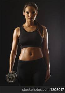 Beautiful toned young woman exercising with a dumbbell over a dark background.