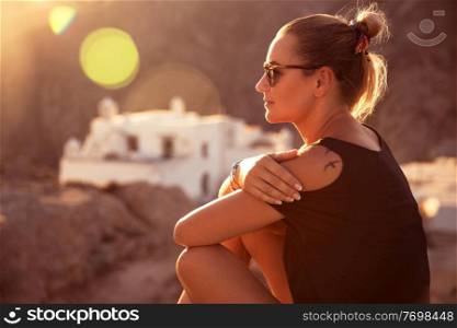 Beautiful traveler girl sitting on top of the mountain and enjoying amazing view on the monastery in sunset light, visiting beautiful places, peaceful spiritual summer vacation