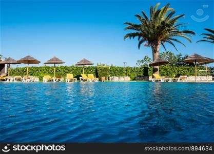 Beautiful tropical beach front hotel resort with swimming pool, sun-loungers and palm trees during a warm sunny day, paradise destination for vacations. Beautiful tropical beach front hotel resort with swimming pool, sun-loungers and palm trees during a warm sunny day.