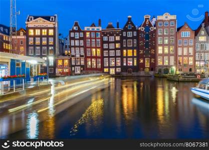 Beautiful typical Dutch dancing houses and tourist boats at the Amsterdam canal Damrak at night, Holland, Netherlands.
