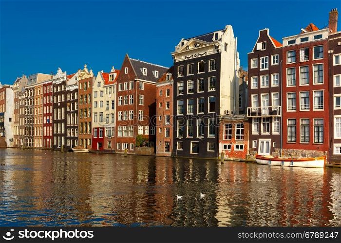 Beautiful typical Dutch dancing houses at the Amsterdam canal Damrak in sunny day, Holland, Netherlands.