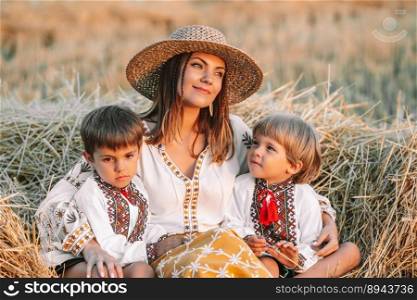 Beautiful ukrainian family - woman and sons in vyshyvanka shirts lying on hay in countryside at sunset. Nature, haystack, vacation, relax and harvest concept. Children, family fun, love. Beautiful ukrainian family - woman sons in vyshyvanka shirts on hay, countryside
