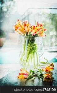 Beautiful unusual mottled red and yellow tulips bunch in glass vase at window with spring nature. Parrot tulips bouquet