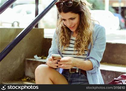 Beautiful urban woman sending message with smartphone on the street.