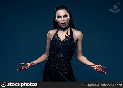 Beautiful vampire style woman in black dress with hands covered in blood