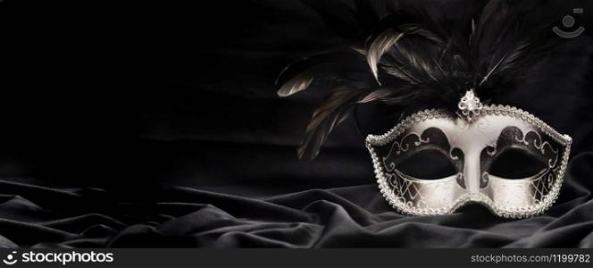 beautiful venitian carnival mask with feather on dark fabric background in panoramic size