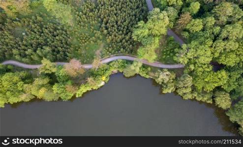 Beautiful view from a road going through the beautiful lake and forest, surrounded with water. Drone photo. Aerial view over sunny lake surrounded by tree forest near town.