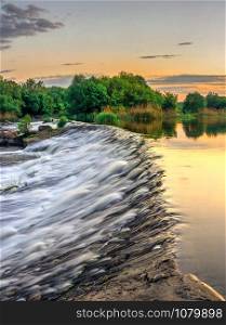 Beautiful view of the dam on the Southern Bug River at sunset. Village of Migiya, Ukraine, on a sunny summer evening. Beautiful view of the dam on the river at sunset